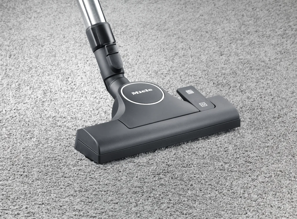 Vacuum floorhead and wand on grey carpet.